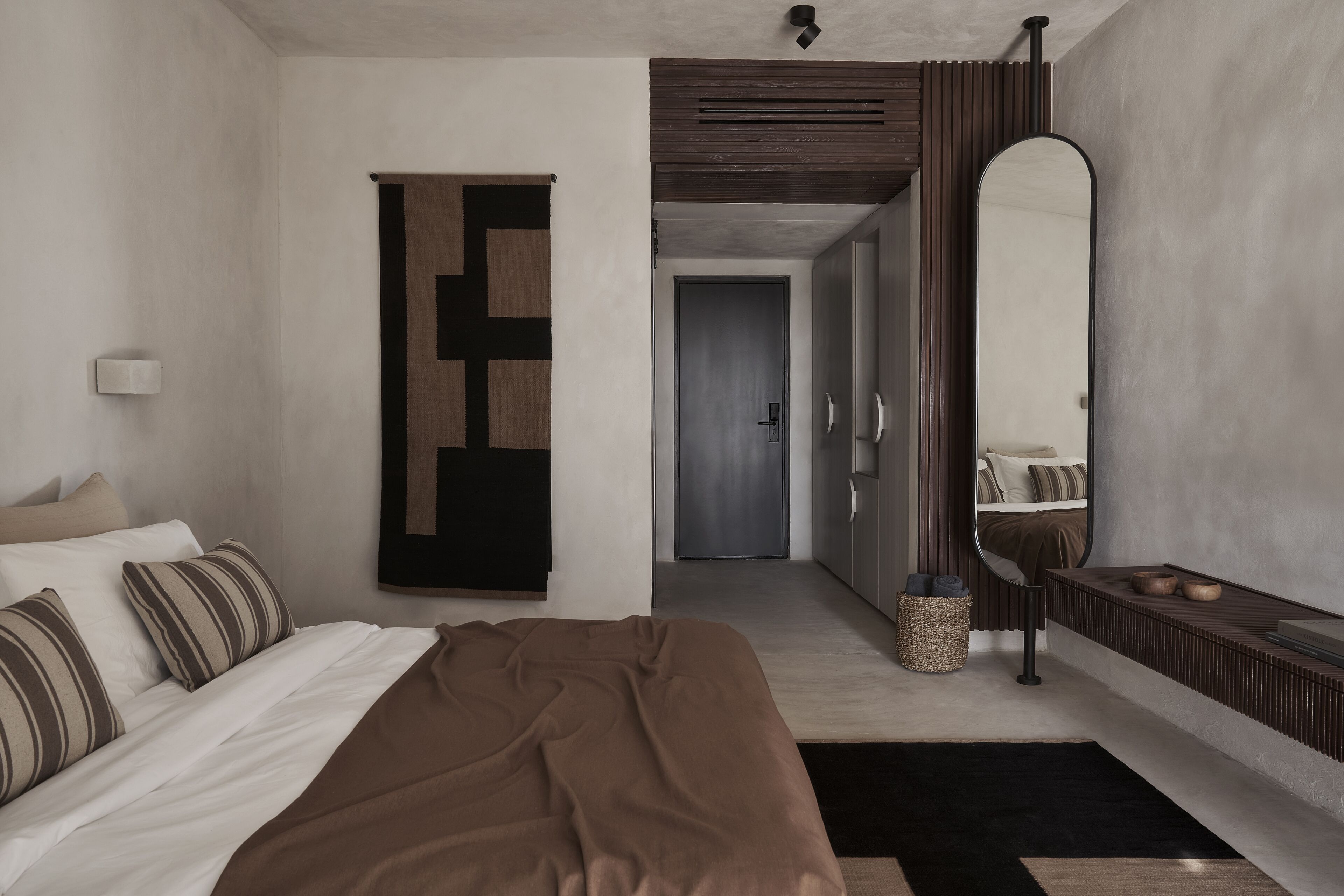 Quarto de hotel moderno com uma cama, um espelho grande, um guarda-roupa e uma porta que dá para outro quarto.