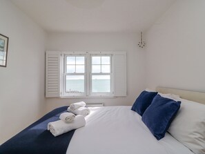 A bedroom with a bed, white linens, blue pillows, and a window with shutters. - Beach Retreat (Weymouth)