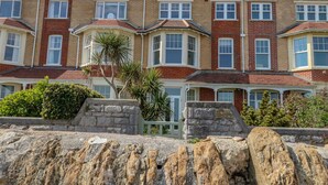 A row of terraced houses with brick facades, bay windows, and a stone wall in the foreground. - Beach Retreat (Weymouth)
