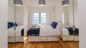 A bedroom with a bed, two bedside tables, a window with shutters, and a view of the sea. - Beach Retreat (Weymouth)
