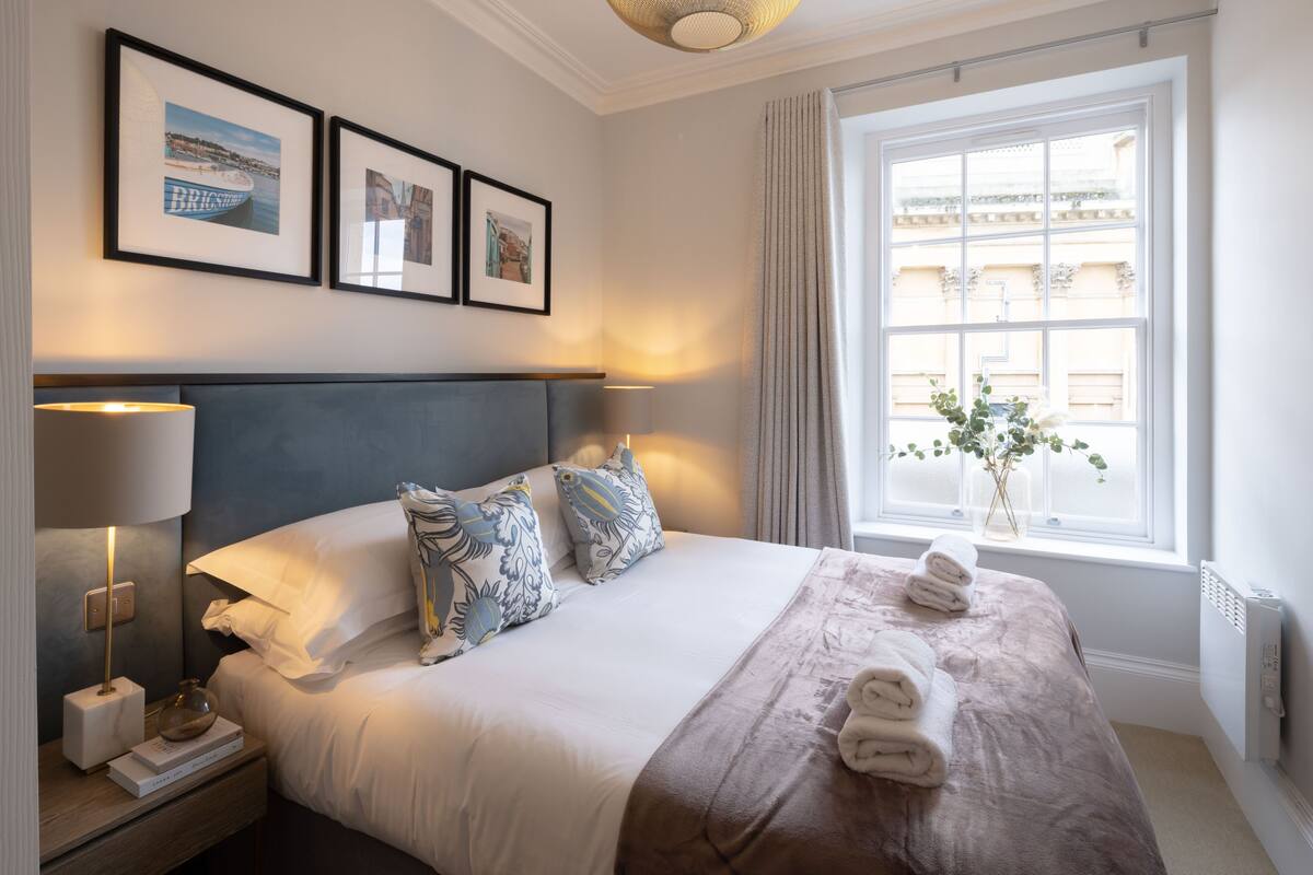 A neatly made bed with pillows, a bedside lamp, and a window with curtains.