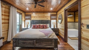 Een houten slaapkamer met een bed, een plafondventilator, een nachtkastje en uitzicht op een badkamer.