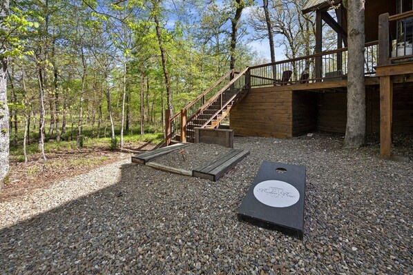 Une terrasse en bois avec un escalier menant à une zone abritée, le tout entouré d’arbres.