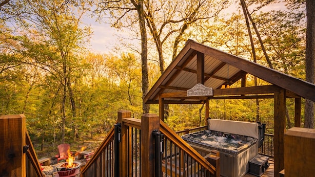 Een houten terras met een jacuzzi en vuurkorf, omgeven door bomen.