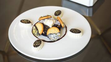 A dessert plate with various sweets and a bowl of fruit in the background.