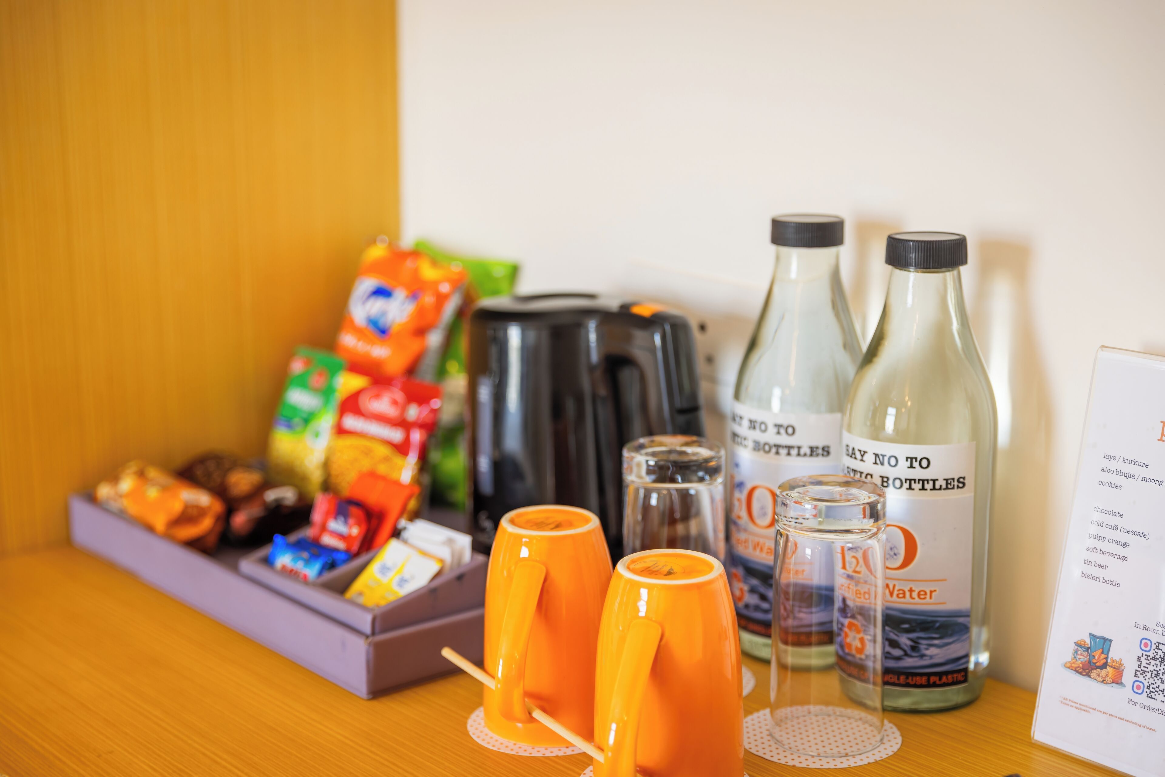 A breakfast setup with orange mugs, a kettle, and bottled water on a wooden table.