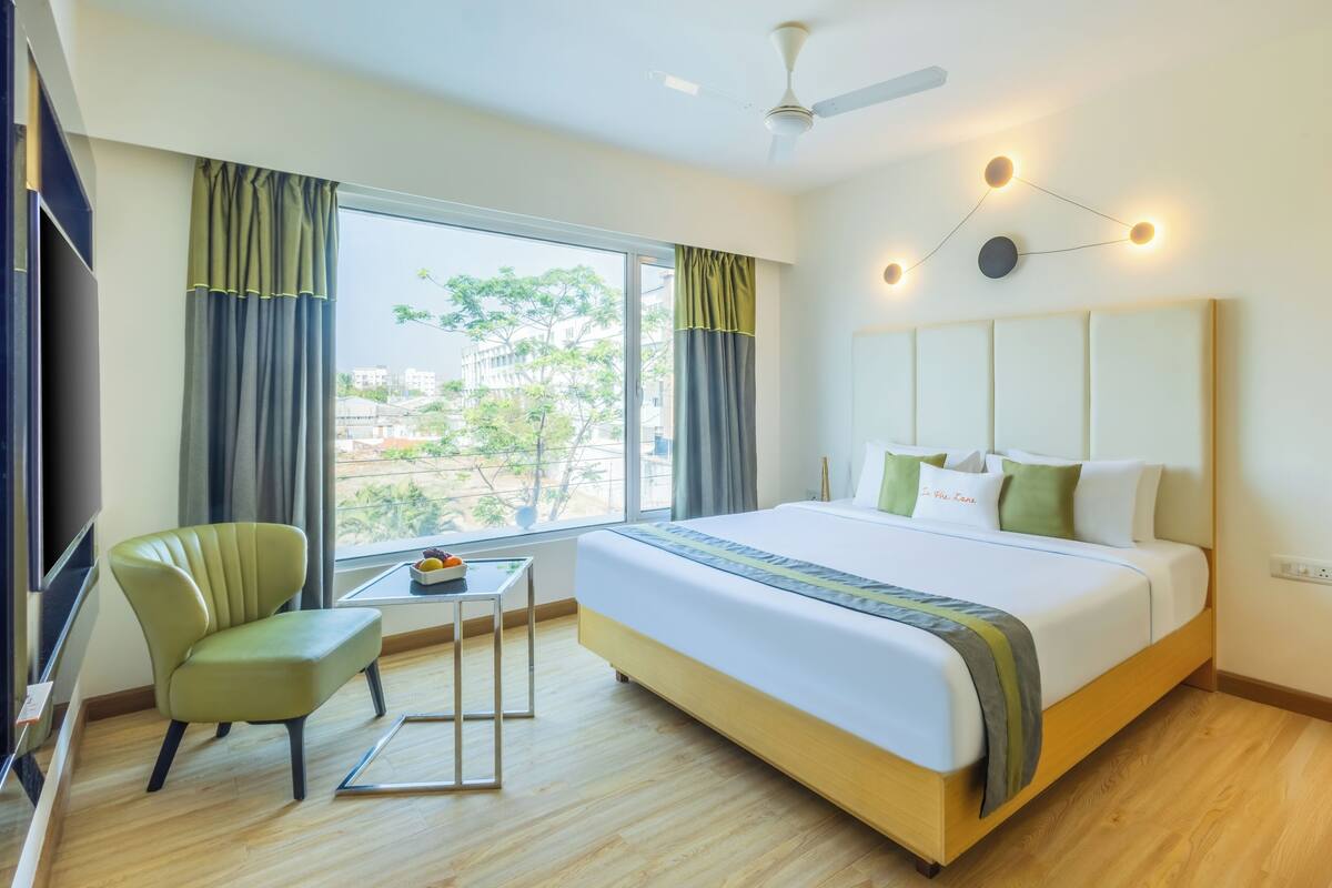 Habitación de hotel con una cama grande, una silla, una mesita y una ventana con cortinas.