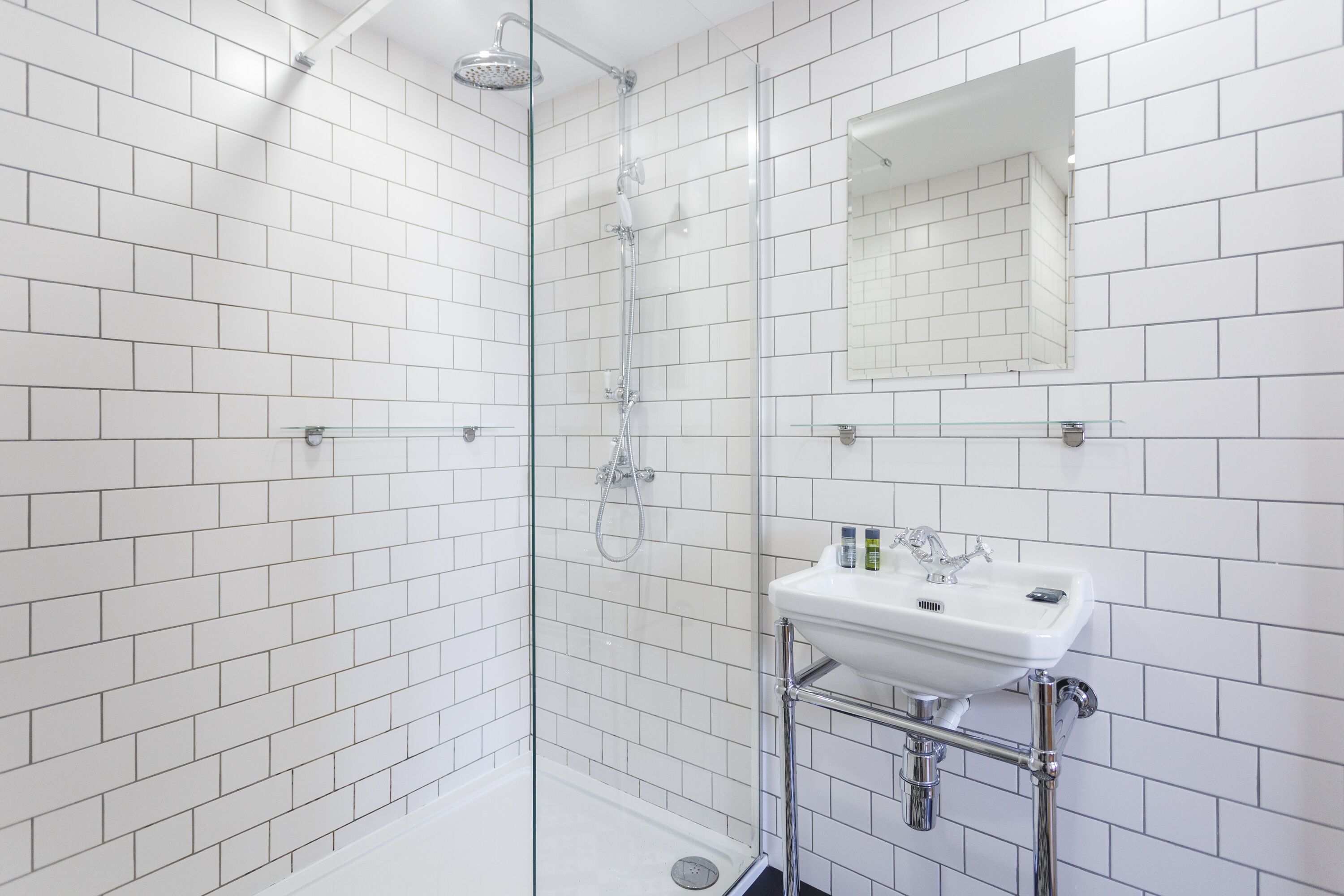A modern bathroom with white subway tiles, a glass-enclosed shower, and a white sink with chrome fixtures.