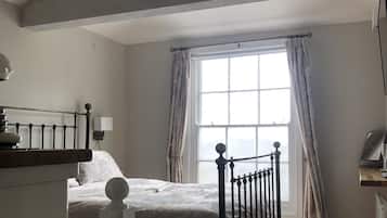 A bedroom with a bed, a wooden floor, a window with curtains, and a ceiling with plants.