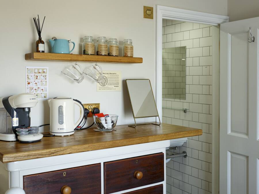 A kitchen with a coffee maker, kettle, and jars on a wooden shelf.