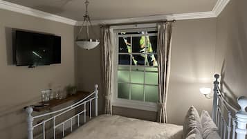 A bedroom with a bed, a TV mounted on the wall, a window with curtains, and a bedside table with a lamp.