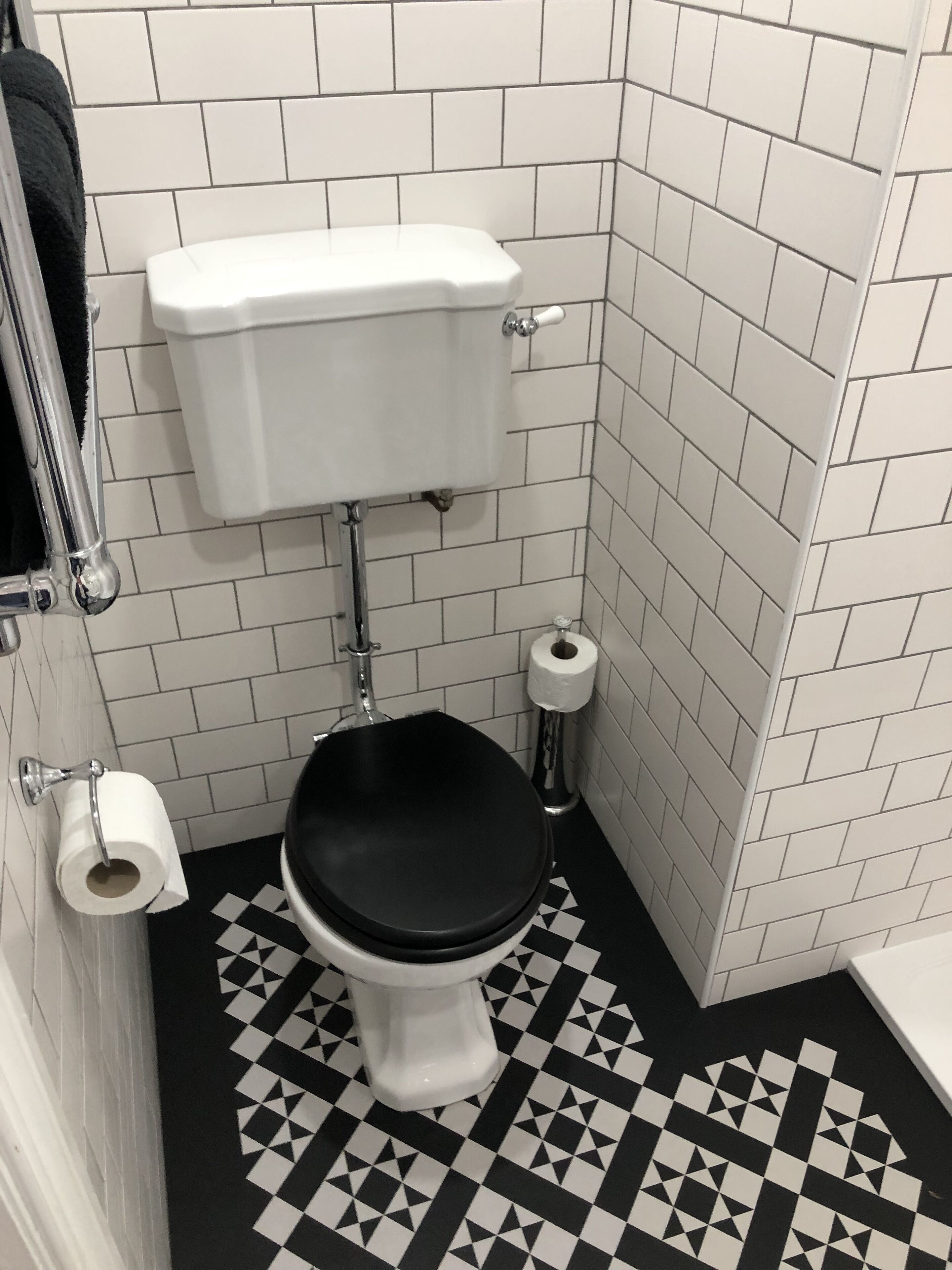 A small bathroom with a toilet, a roll of toilet paper, and a black and white patterned floor.