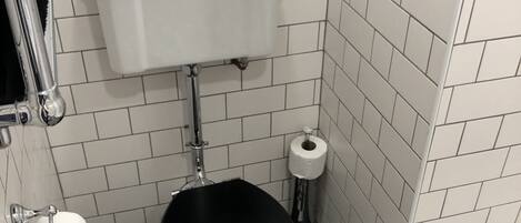 Un baño pequeño con inodoro, un rollo de papel higiénico y un suelo con estampado blanco y negro.