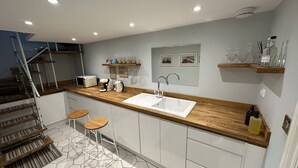 Una cocina moderna con encimera de madera, armarios blancos, un lavamanos empotrado y suelo de baldosas hexagonales.