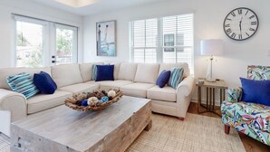 Una sala moderna con un sofá beige, una mesa de centro con bolas decorativas, un sillón colorido y un reloj de pared grande.
