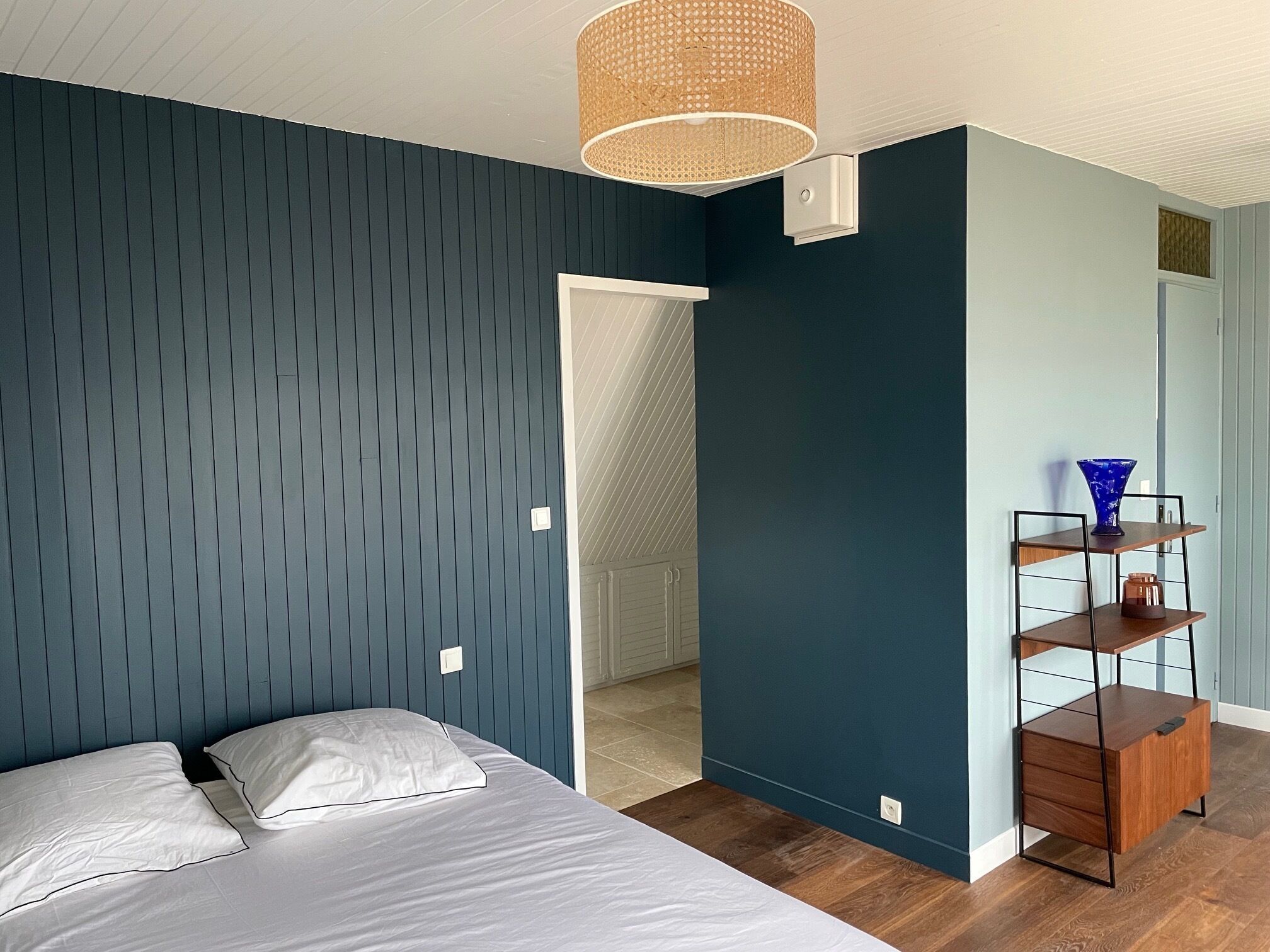 Un dormitorio con una cama, una estantería en la pared y una puerta que da a otra habitación.