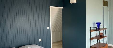 Un dormitorio con una cama, una estantería en la pared y una puerta que da a otra habitación.