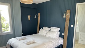 A neatly made bed with white linens and two towels, a wooden headboard, and a wall-mounted light fixture.