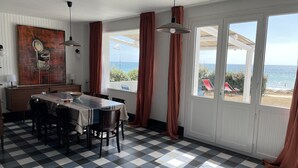 A dining area with a checkered floor, a table with chairs, a painting on the wall, and large windows with curtains.