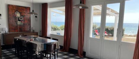 Un comedor con suelo a cuadros, una mesa con sillas, un cuadro en la pared y ventanas grandes con cortinas.