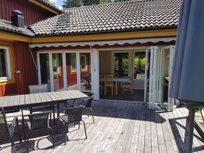 A wooden deck with a table and chairs, a covered patio area, and a building with a tiled roof and red siding. - Spacious two-story villa on a fenced lot in the Isaberg recreational area (Hestra)