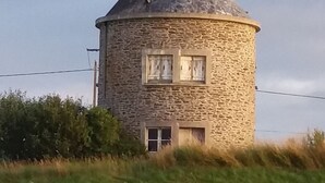 A stone tower with a conical roof, surrounded by tall grass and bushes. - Spacious and quiet house (LA FRESNAIS)