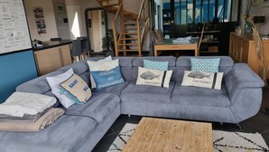 A modern living room with a grey sectional sofa, multiple cushions, a wooden coffee table, and a staircase leading to another level. - Spacious and quiet house (LA FRESNAIS)