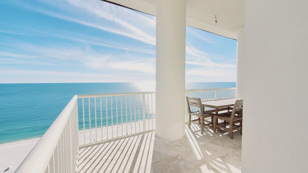 A balcony with a view of the ocean, a table with chairs, and a white railing.