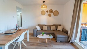 A modern living room with a grey sofa, a wooden dining table with chairs, a small round table with plants, and a hanging light fixture.