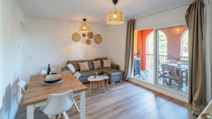 A modern living room with a wooden dining table, white chairs, a sofa, and a balcony with a table and chairs.