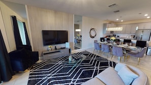 Ein modernes Wohnzimmer mit Flachbildfernseher, Glastisch und einem schwarz-weißen Teppich.