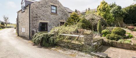 A stone house with a sloped roof, a small window, and a stone wall with greenery.