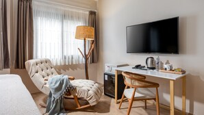 A modern hotel room with a large bed, a comfortable armchair, a desk with a computer, a television, and a small kitchenette. - Gran Via Alsancak (Izmir)