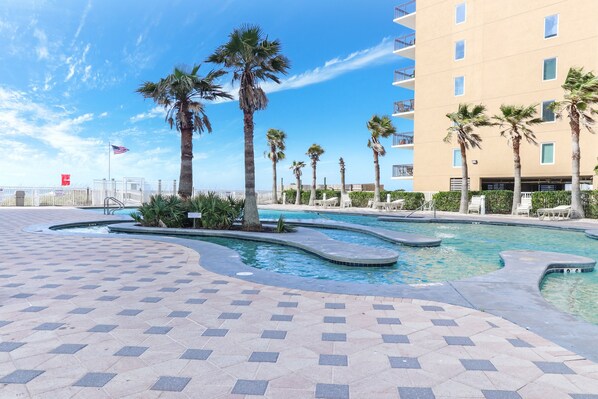 Relax by the resort pool surrounded by palm trees and a building with balconies.
