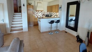 A spacious living area with a sofa, a kitchen with wooden cabinets, a dining area with a mirror, and a staircase leading to another level. - Villa Golf Saint Endréol La Motte (La Motte)
