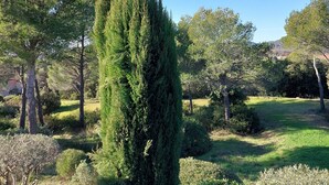 A well-maintained garden with a variety of trees and shrubs, a clear sky, and a distant view of hills. - Villa Golf Saint Endréol La Motte (La Motte)