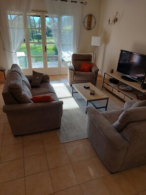 A living room with two sofas, a coffee table, a TV, and a large window with curtains. - Villa Golf Saint Endréol La Motte (La Motte)