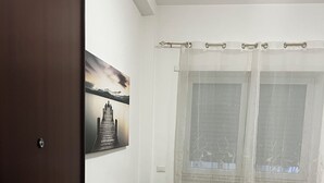A room with a beige sofa, a wooden floor, a door with a brass handle, a window with sheer curtains, and a painting on the wall. - Apartment in St. Peter  (Roma)