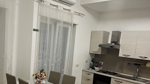 A modern kitchen with a built-in stove, sink, and cabinets. There is a dining table with chairs and a vase of flowers. - Apartment in St. Peter  (Roma)