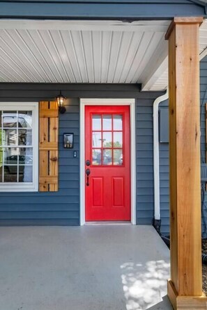 A house with a red door, a wooden window shutter, and a porch with a concrete floor. - Charming cottage north of Gastonia — stylish, comfy retreat near local amenities (Dallas)