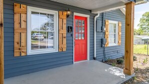 Une maison avec une porte rouge, des fenêtres à cadre blanc et des volets en bois.