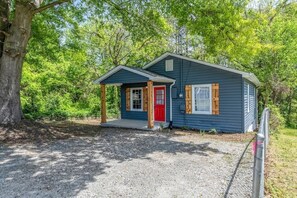 Une petite cabane à un seul étage, avec une porte rouge et des volets en bois, entourée d’arbres.