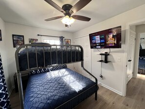 Une chambre avec un lit superposé, un ventilateur de plafond, un téléviseur fixé au mur et une porte donnant sur une autre pièce.