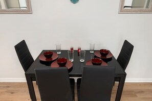 Une table à manger dressée pour quatre personnes, avec des chaises noires, des assiettes rouges et des verres transparents.