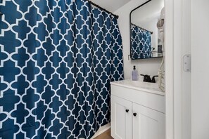 Une salle de bain avec un meuble-lavabo blanc, un miroir et un rideau de douche bleu à motifs.