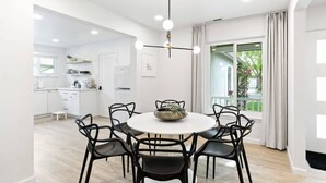 Un comedor moderno con una mesa redonda y sillas negras, una lámpara colgante y vistas a un jardín a través de un ventanal.