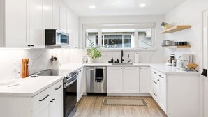 Una cocina moderna con gabinetes blancos, lavavajillas de acero inoxidable y una ventana sobre el fregadero.