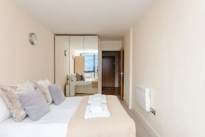 A hotel room with a bed, a mirror, a radiator, and a door leading to another room.