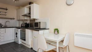 A modern kitchen with white cabinetry, a built-in oven, a microwave, and a dining area with a table and chairs. - Vivid Apartment in Central London (London)