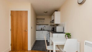 A compact kitchen with white cabinets, a black countertop, and a small dining area with a white table and chairs. - Vivid Apartment in Central London (London)